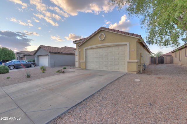 view of front facade with a tile roof, concrete driveway, stucco siding, fence, and an attached garage