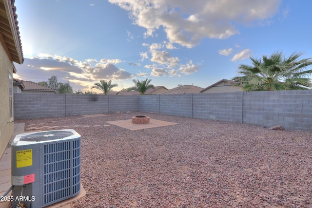 yard at dusk featuring an outdoor fire pit, central AC, a patio area, and a fenced backyard