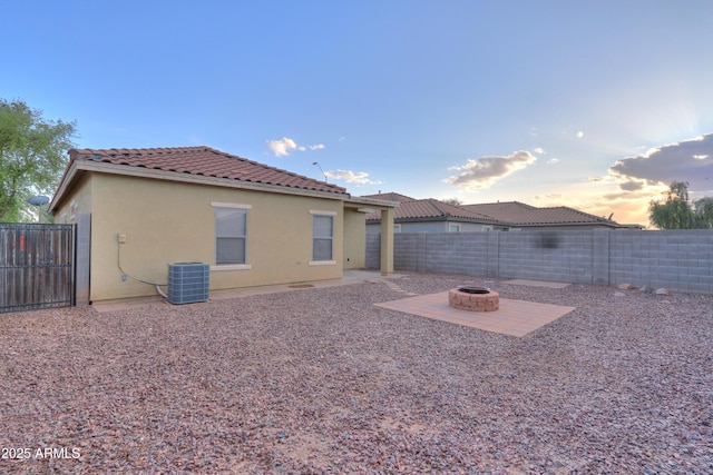 back of property with central AC unit, a tiled roof, an outdoor fire pit, a fenced backyard, and stucco siding