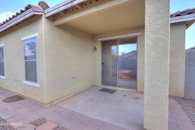 entrance to property featuring stucco siding, a tile roof, and a patio