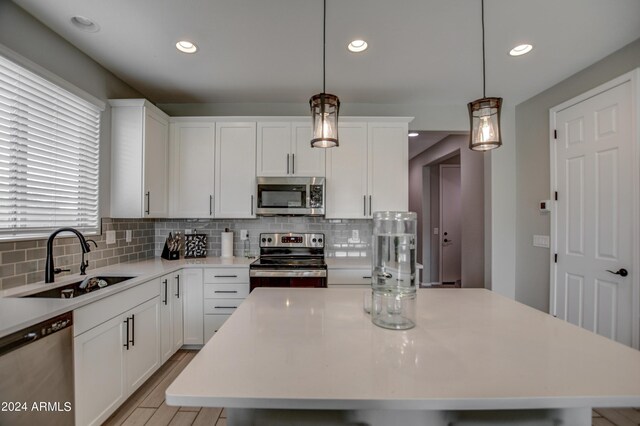 kitchen featuring a center island, hanging light fixtures, stainless steel appliances, white cabinets, and sink