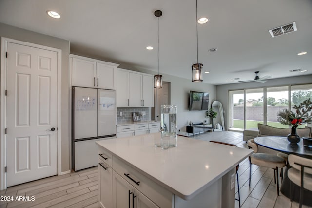 kitchen featuring white fridge, backsplash, white cabinetry, a center island, and pendant lighting