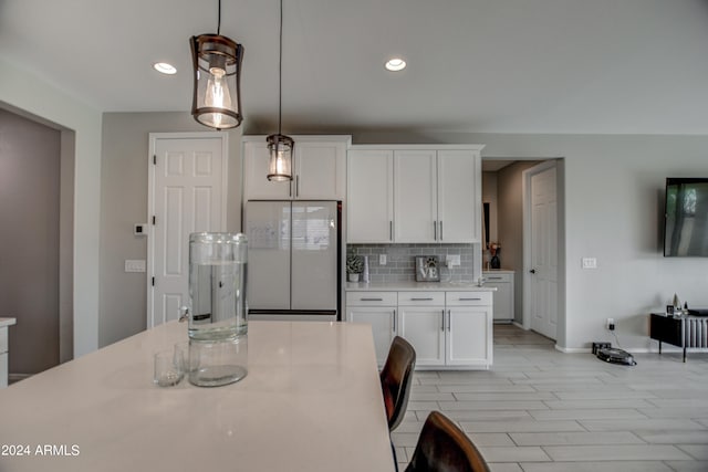 kitchen featuring white cabinets, stainless steel fridge, decorative light fixtures, and backsplash