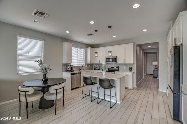 kitchen featuring backsplash, a center island, pendant lighting, white cabinets, and appliances with stainless steel finishes