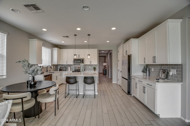 kitchen featuring backsplash, appliances with stainless steel finishes, white cabinets, and decorative light fixtures