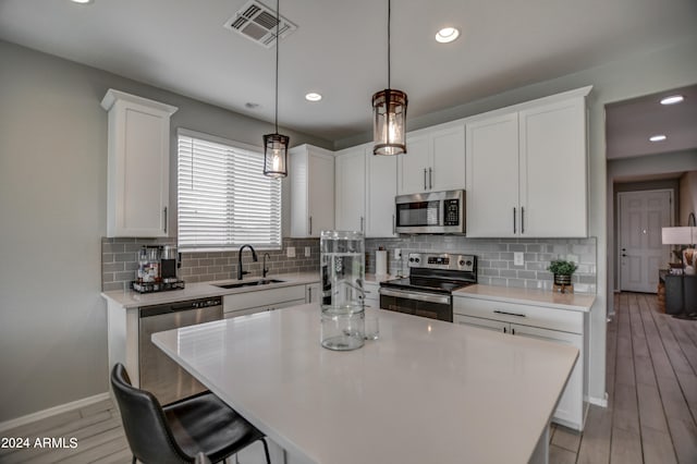 kitchen with appliances with stainless steel finishes, sink, white cabinets, and a kitchen island