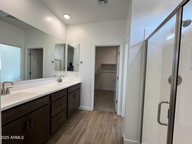 bathroom with a sink, visible vents, wood finish floors, and a shower stall