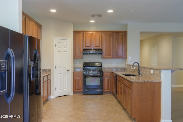 kitchen featuring kitchen peninsula, a kitchen bar, light stone counters, sink, and black appliances