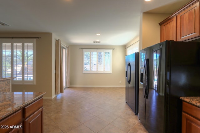 kitchen with stainless steel fridge, light stone countertops, black fridge with ice dispenser, and light tile patterned flooring