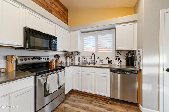 kitchen with dark countertops, decorative backsplash, appliances with stainless steel finishes, a sink, and wood finished floors