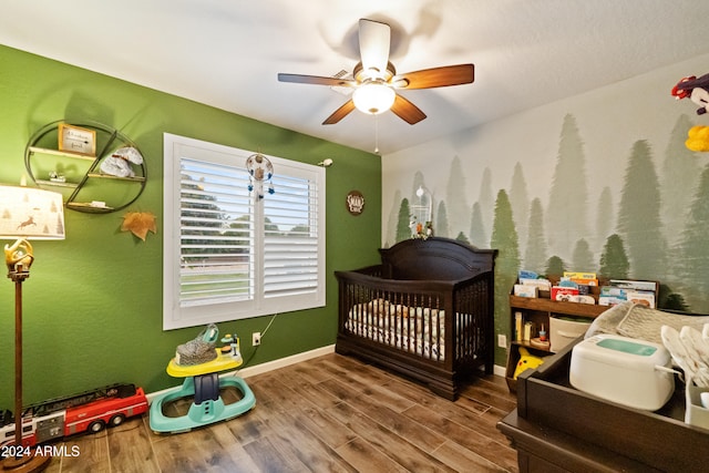 bedroom with a nursery area, ceiling fan, baseboards, and wood finished floors