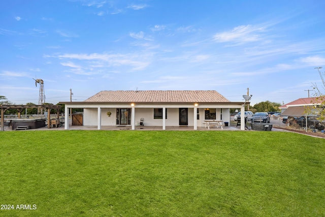 rear view of property with a hot tub, a tiled roof, a lawn, and a patio