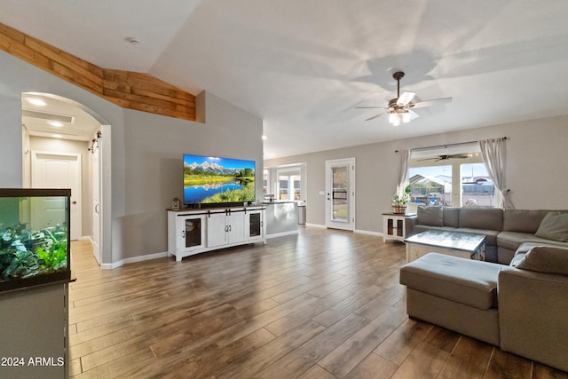 living area with lofted ceiling, arched walkways, wood finished floors, and baseboards