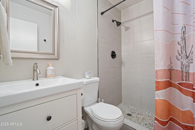 bathroom featuring vanity, toilet, a textured wall, and tiled shower