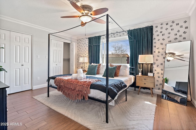 bedroom featuring two closets, ceiling fan, baseboards, ornamental molding, and wood finished floors