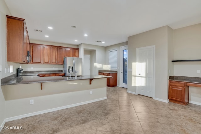 kitchen featuring sink, a breakfast bar area, stove, stainless steel refrigerator with ice dispenser, and kitchen peninsula