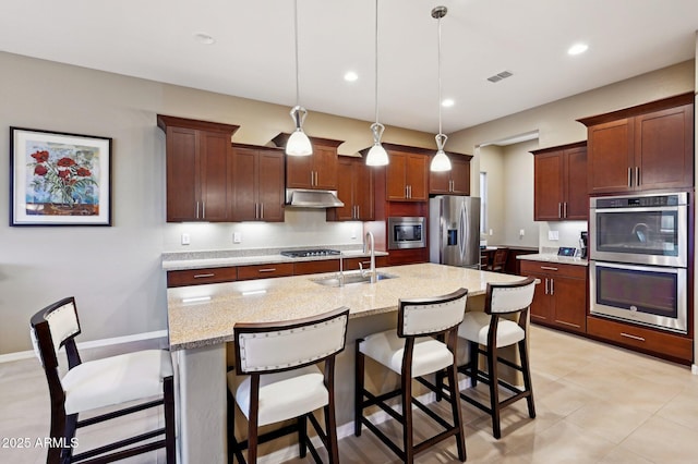 kitchen with decorative light fixtures, stainless steel appliances, light stone counters, and sink