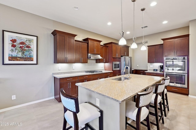 kitchen featuring stainless steel appliances, sink, a center island with sink, hanging light fixtures, and a breakfast bar area