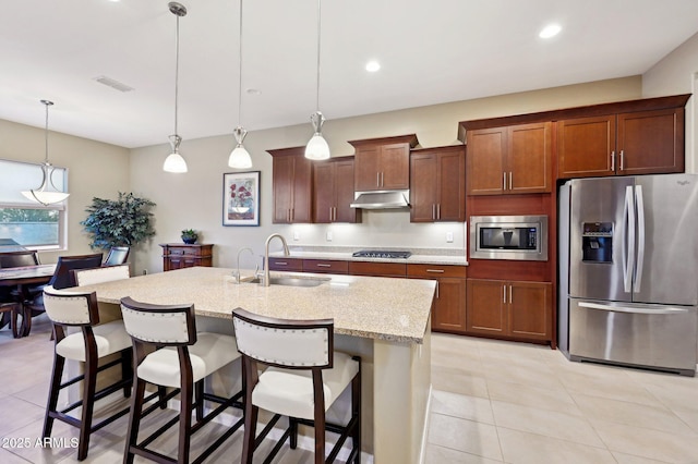 kitchen with a kitchen breakfast bar, stainless steel appliances, a kitchen island with sink, sink, and decorative light fixtures