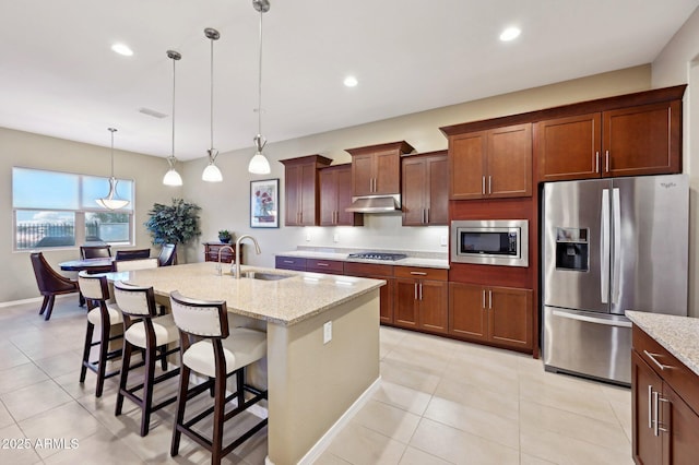 kitchen featuring light stone counters, a center island with sink, pendant lighting, and appliances with stainless steel finishes