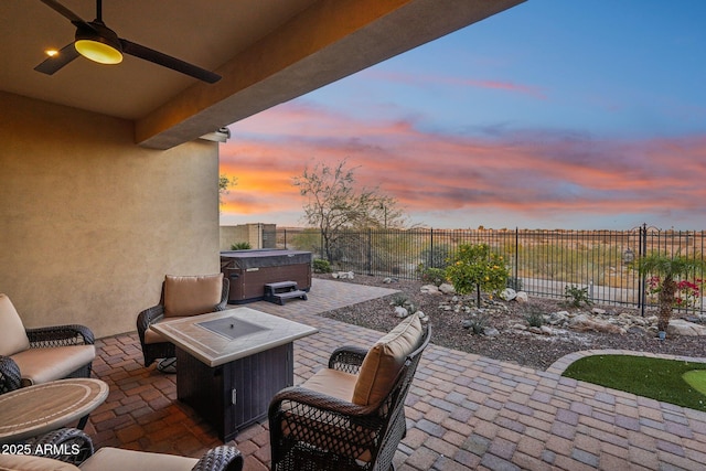 patio terrace at dusk with ceiling fan, an outdoor fire pit, and a hot tub