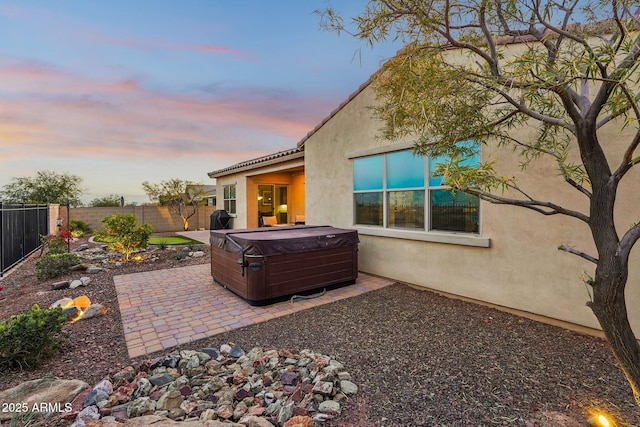 back house at dusk with a hot tub and a patio area