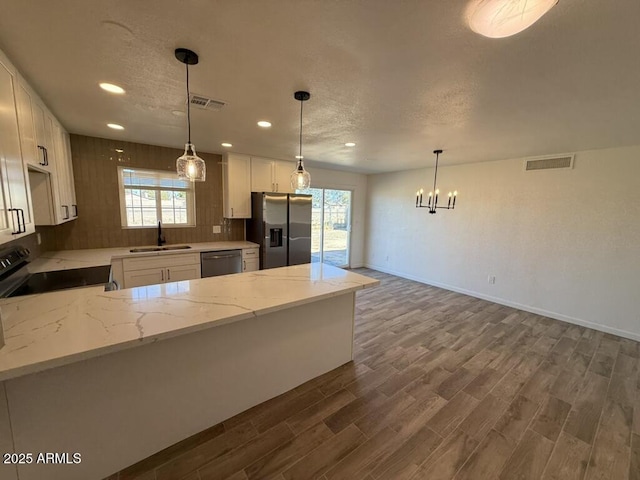 kitchen with appliances with stainless steel finishes, white cabinetry, sink, decorative light fixtures, and light stone counters