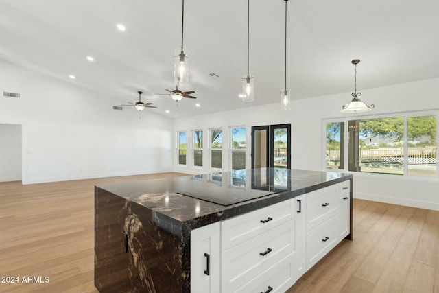 kitchen with light wood-type flooring, a center island, plenty of natural light, and dark stone counters