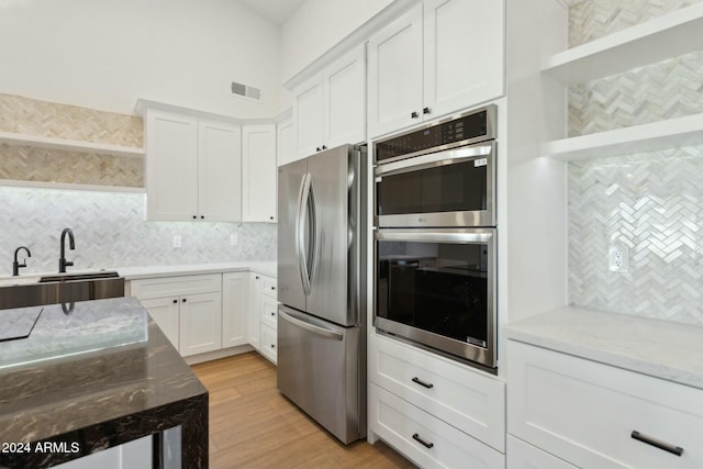 kitchen with light stone countertops, stainless steel appliances, sink, light hardwood / wood-style flooring, and white cabinets