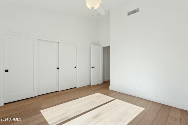 unfurnished bedroom featuring ceiling fan, a closet, a high ceiling, and light wood-type flooring