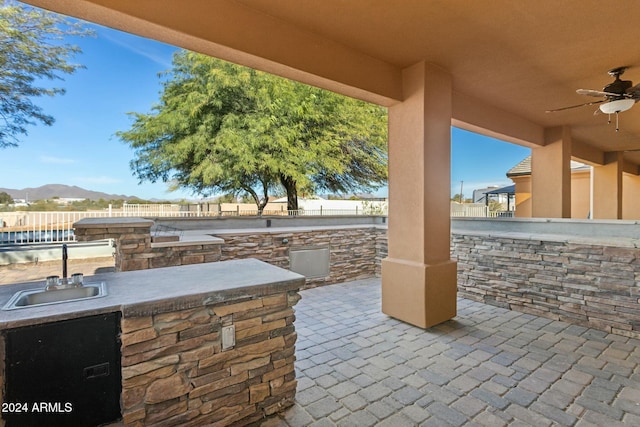 view of patio / terrace with ceiling fan, sink, an outdoor kitchen, a grill, and a mountain view