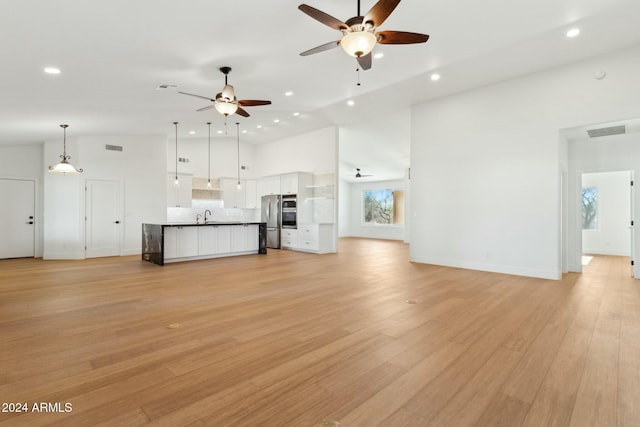 unfurnished living room featuring sink, high vaulted ceiling, and light wood-type flooring