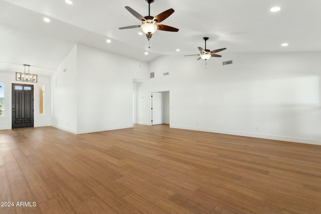 unfurnished living room featuring ceiling fan with notable chandelier, light wood-type flooring, and high vaulted ceiling