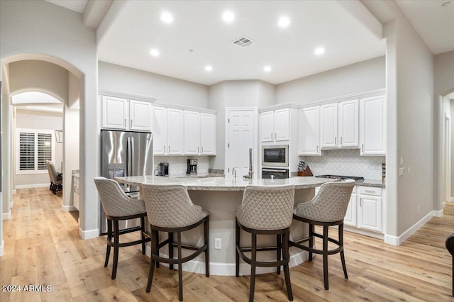 kitchen with a kitchen breakfast bar, white cabinetry, a kitchen island with sink, and light hardwood / wood-style flooring