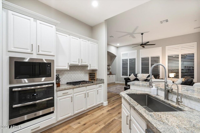 kitchen featuring stainless steel appliances, sink, light stone countertops, white cabinetry, and light hardwood / wood-style flooring