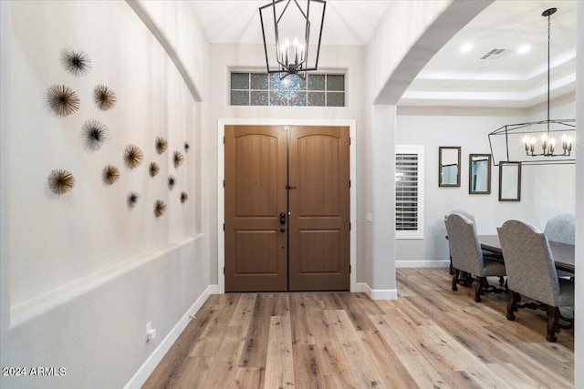 foyer with light wood-type flooring, a notable chandelier, and a tray ceiling