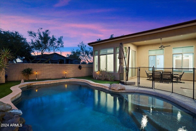 pool at dusk with ceiling fan and a patio area