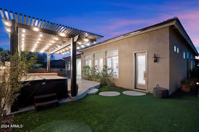 back house at dusk with a yard, a hot tub, a pergola, and a patio area