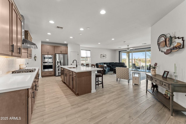 kitchen featuring a breakfast bar, sink, an island with sink, appliances with stainless steel finishes, and extractor fan