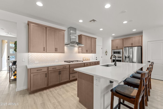 kitchen with wall chimney exhaust hood, a breakfast bar, stainless steel appliances, sink, and an island with sink