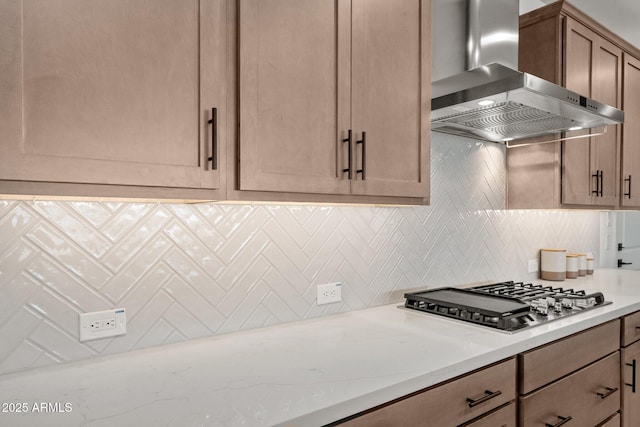 kitchen featuring decorative backsplash, light stone counters, wall chimney exhaust hood, and stainless steel gas stovetop