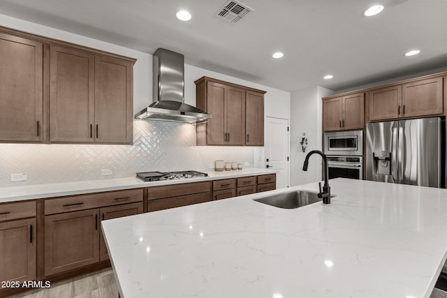 kitchen with decorative backsplash, appliances with stainless steel finishes, light stone countertops, wall chimney exhaust hood, and sink