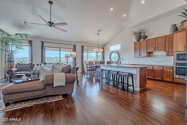 living area featuring dark wood-style floors, visible vents, high vaulted ceiling, and ceiling fan with notable chandelier