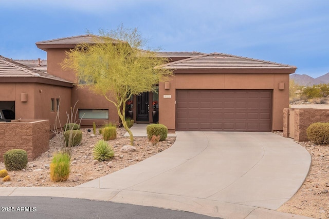 view of front of home featuring driveway, an attached garage, a tile roof, and stucco siding