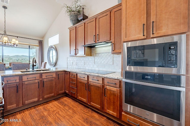 kitchen featuring built in microwave, black electric cooktop, under cabinet range hood, stainless steel oven, and a sink