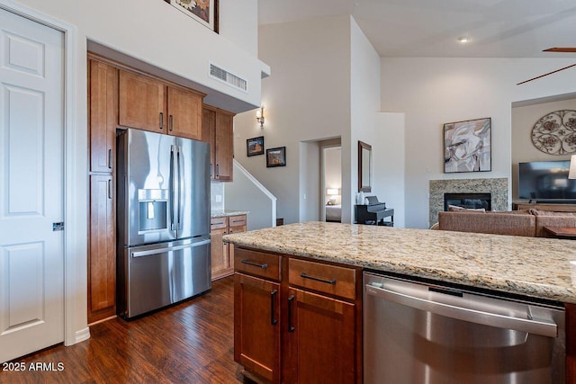 kitchen featuring visible vents, appliances with stainless steel finishes, brown cabinets, light stone counters, and dark wood-style flooring