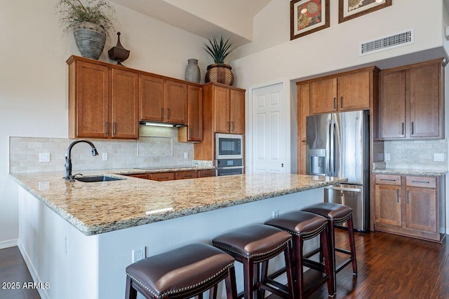 kitchen featuring a peninsula, a sink, visible vents, appliances with stainless steel finishes, and brown cabinetry