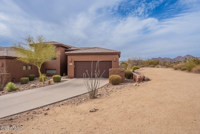 view of front facade with an attached garage, a mountain view, concrete driveway, and stucco siding