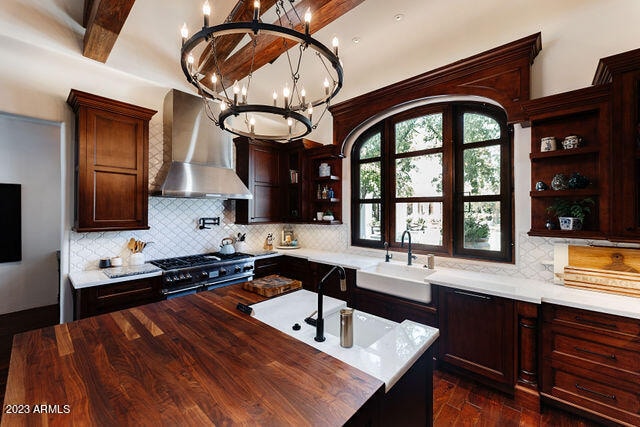 kitchen with an inviting chandelier, a center island, wall chimney exhaust hood, butcher block countertops, and sink