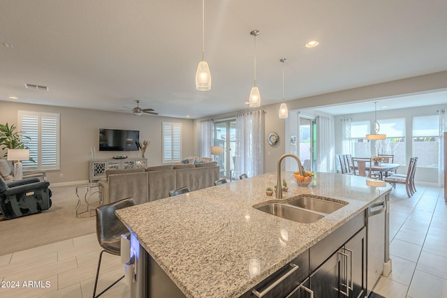 kitchen with light stone countertops, light carpet, sink, pendant lighting, and an island with sink